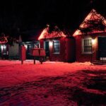 A cozy brick house exterior with red neon lights glowing at night during winter, enhancing the snowy landscape.