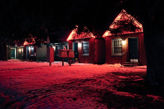 A cozy brick house exterior with red neon lights glowing at night during winter, enhancing the snowy landscape.