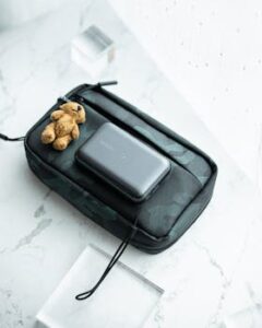 Black gadget pouch with charger and teddy bear on a marble surface.