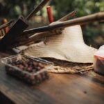 A close-up of gardening tools and a straw hat on a rustic wooden table, evoking a warm, outdoor garden setting.