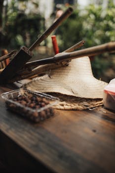 A close-up of gardening tools and a straw hat on a rustic wooden table, evoking a warm, outdoor garden setting.