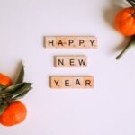 Happy New Year message with Scrabble tiles and fresh mandarins for festive decor.