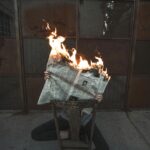 A stunning photo of a newspaper on fire, held by a person with a dark background.