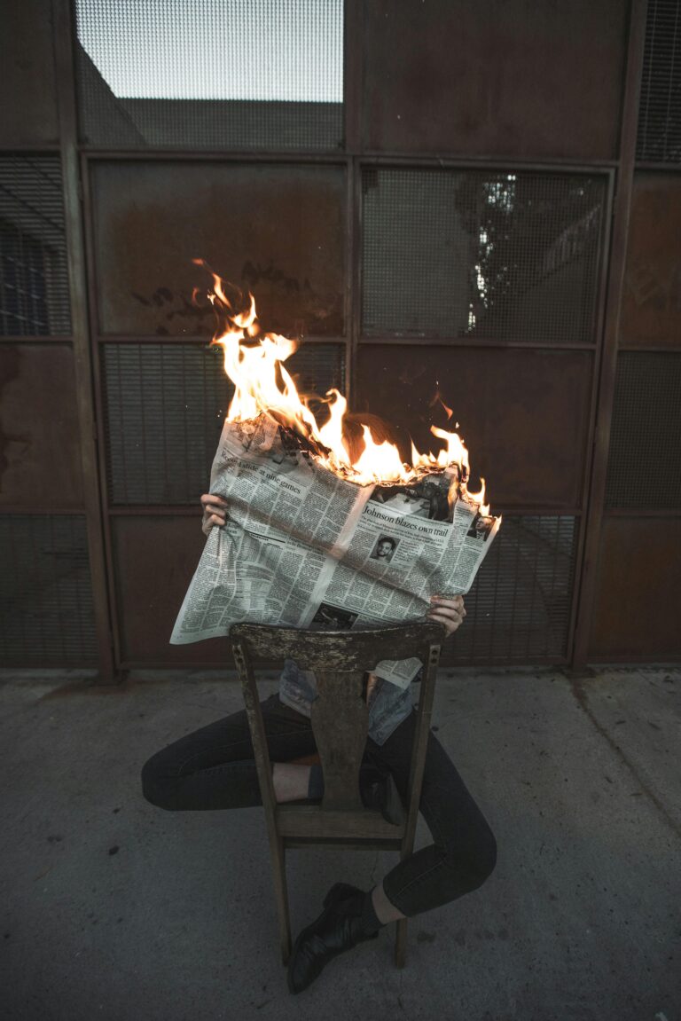 A stunning photo of a newspaper on fire, held by a person with a dark background.