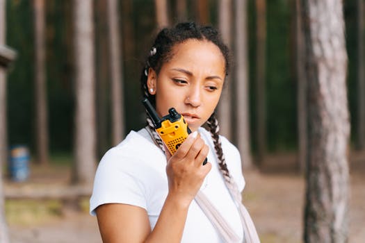 Focused young woman communicates using a two-way radio in an outdoor forest setting.