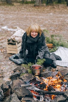 Woman enjoying a peaceful moment cooking by a campfire in the forest.