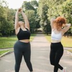Two women stretching in a park, embracing wellness and fitness in comfortable activewear.
