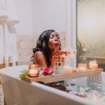 A serene woman enjoys a relaxing spa bath surrounded by candles and flowers.