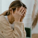 A woman sitting indoors covering her face in frustration, depicting stress and mental health challenges.