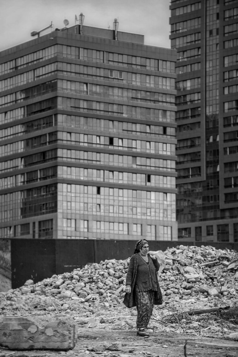A lone woman walking through rubble with towering skyscrapers in the background, conveying urban resilience.