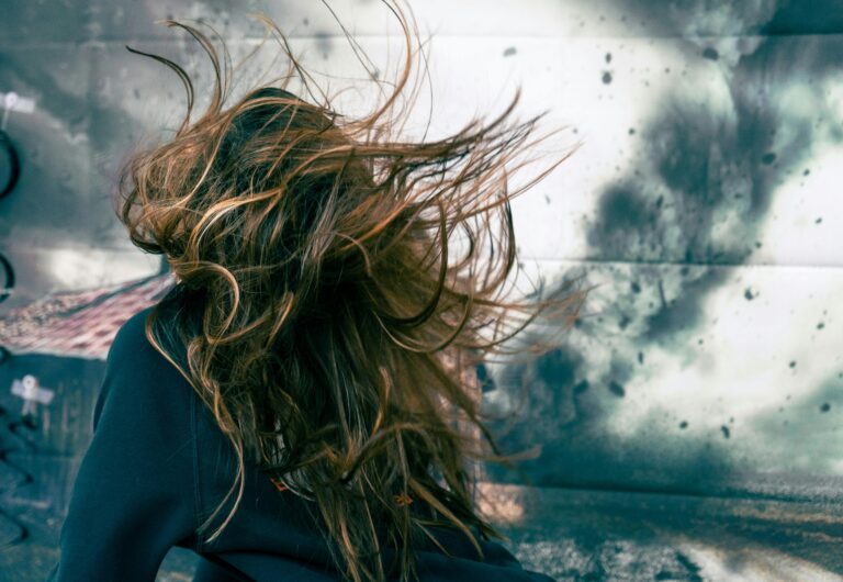 A woman with disheveled hair caught in strong wind against a stormy backdrop, capturing motion and chaos.