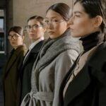 Group of diverse women in fashionable coats and glasses exuding confidence and style.