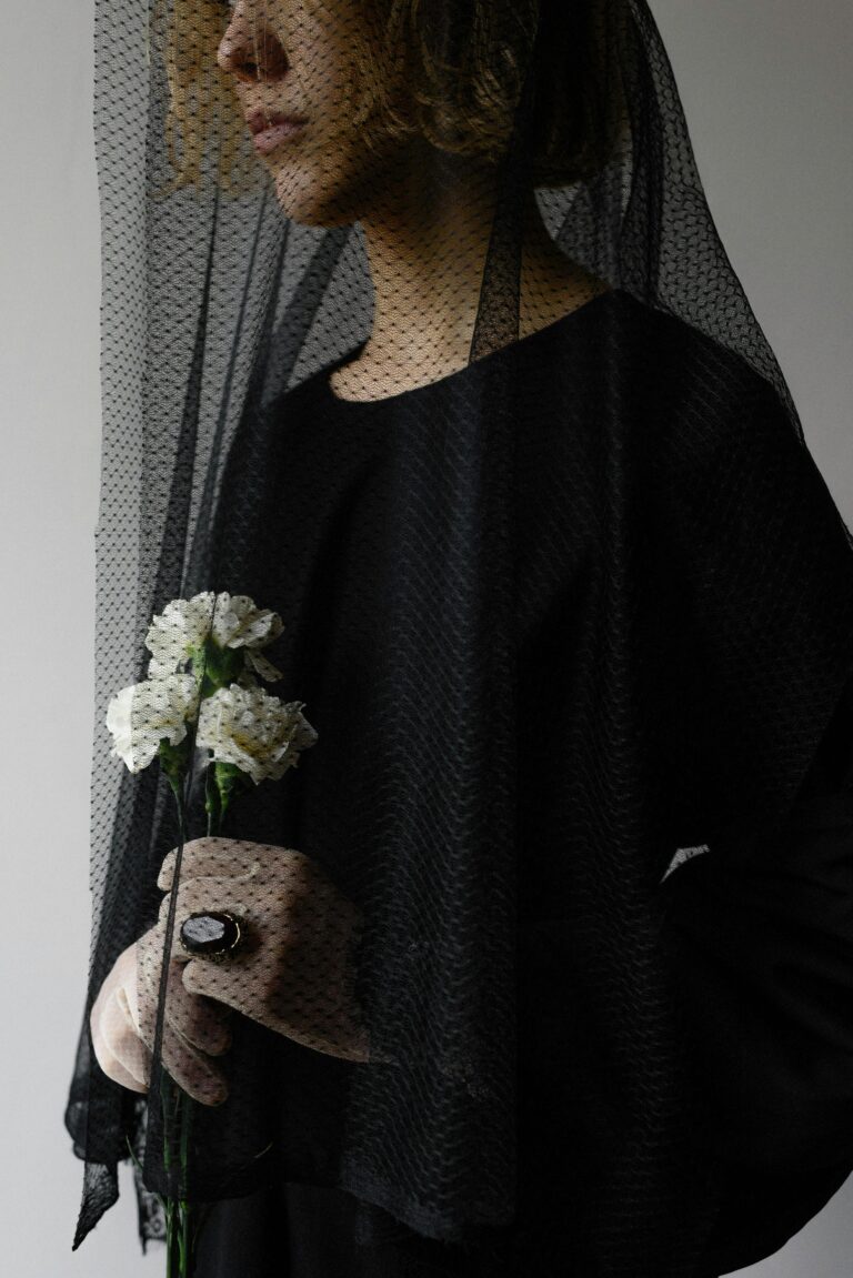 A woman wearing a black veil holds white flowers in a solemn, indoor setting.