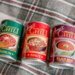 Three varieties of Amy's Organic Chili cans on a plaid picnic blanket.