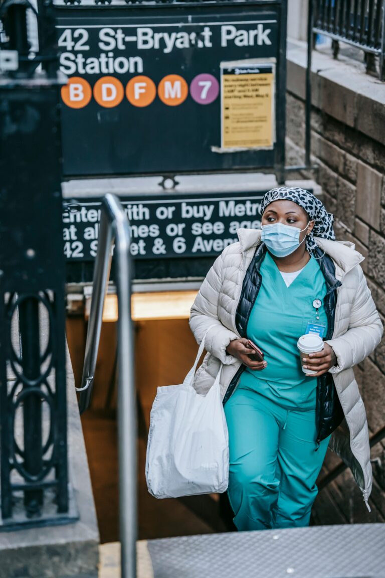 Contemplative African American nurse in outerwear and face mask carrying takeaway coffee and leaving New York metro station while commuting to work